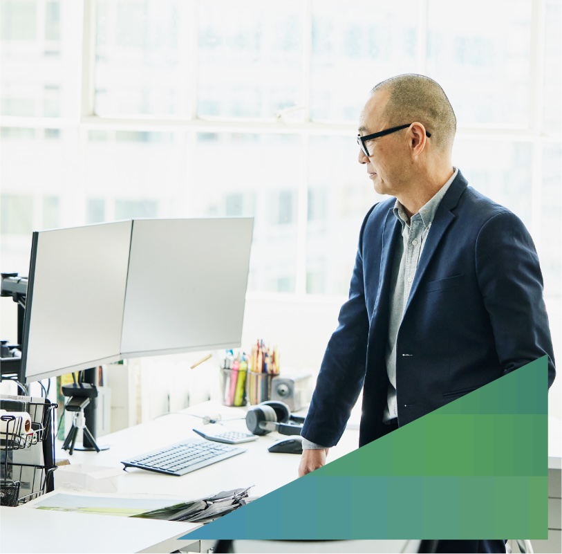 Businessman looks at a pair of computer monitors at his office work desk