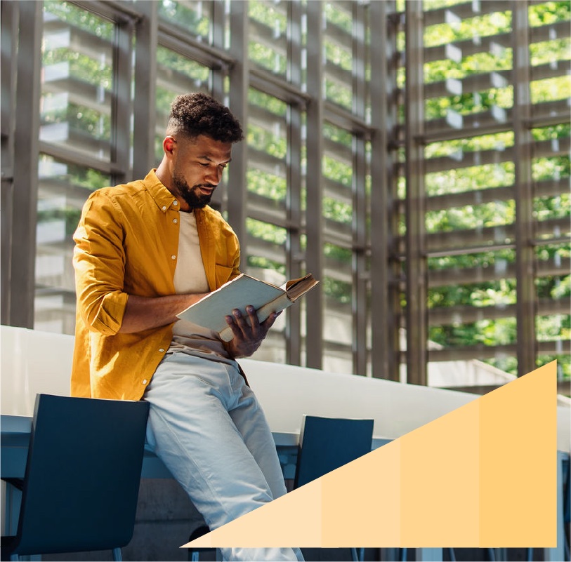 Young Black professional reading a book in a large naturally lit office lobby.