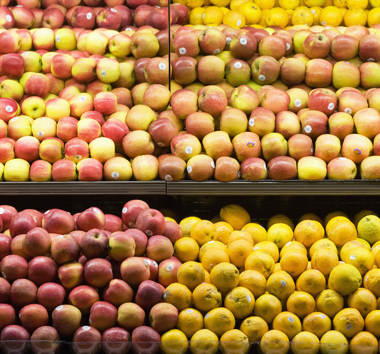 Apples and oranges are organized and arranged colorfully and appealingly on shelves in a supermarket.