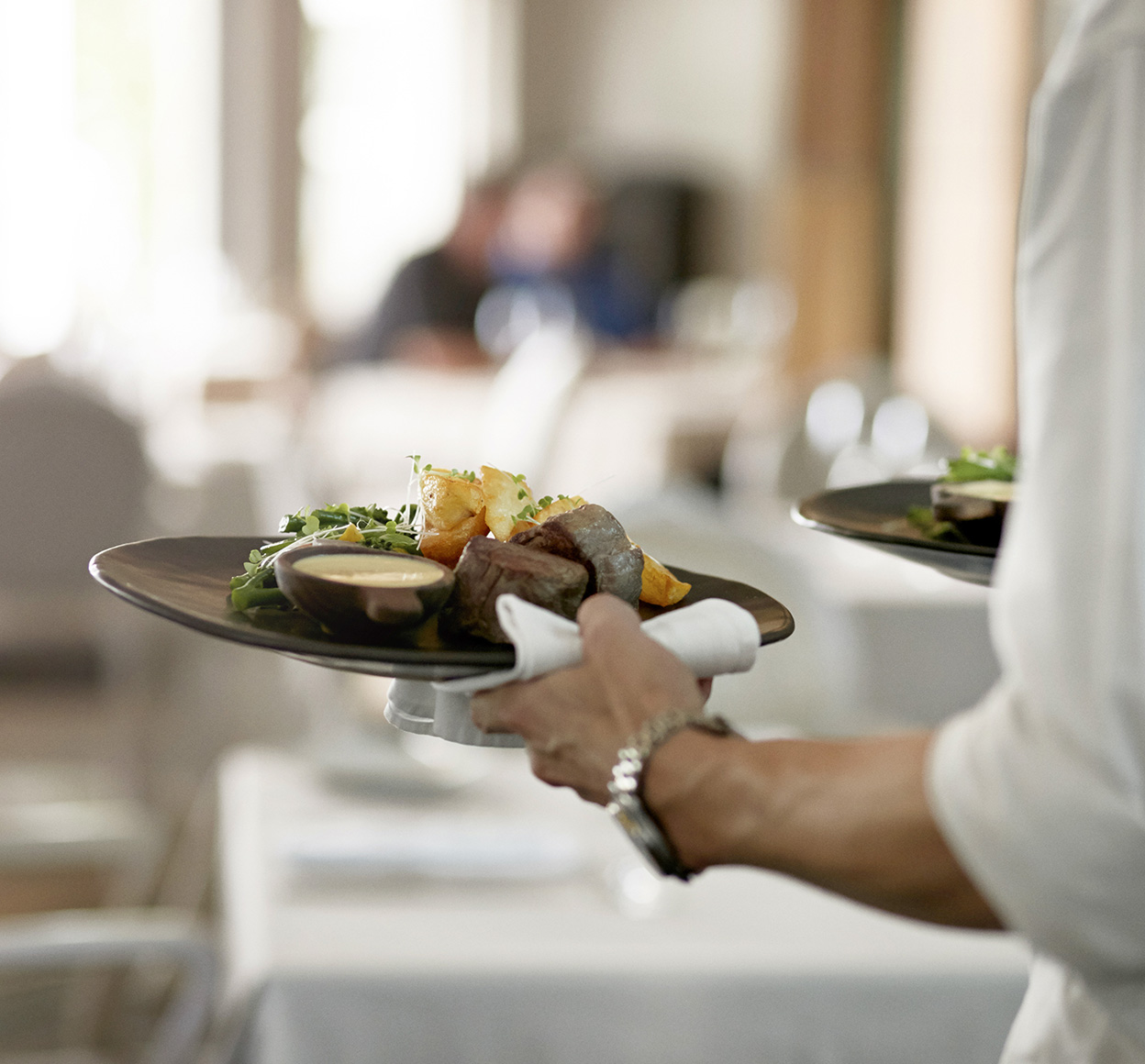Close-up of waiter serving plate of food