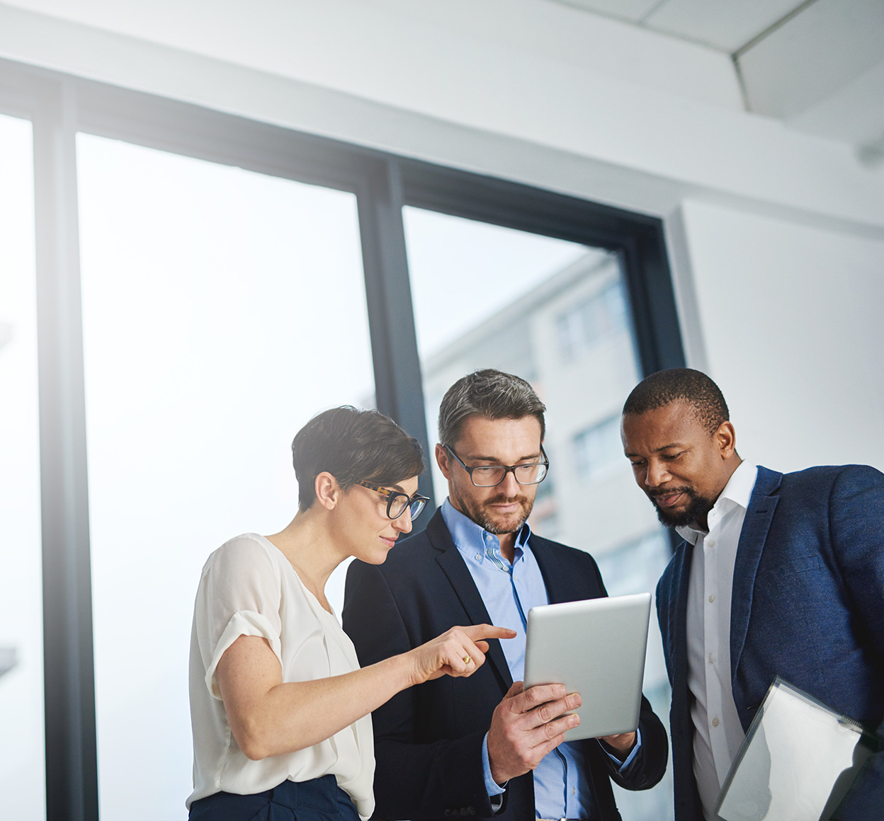 A team of colleagues collaborating on a tablet, working towards a common goal in front of an office window.