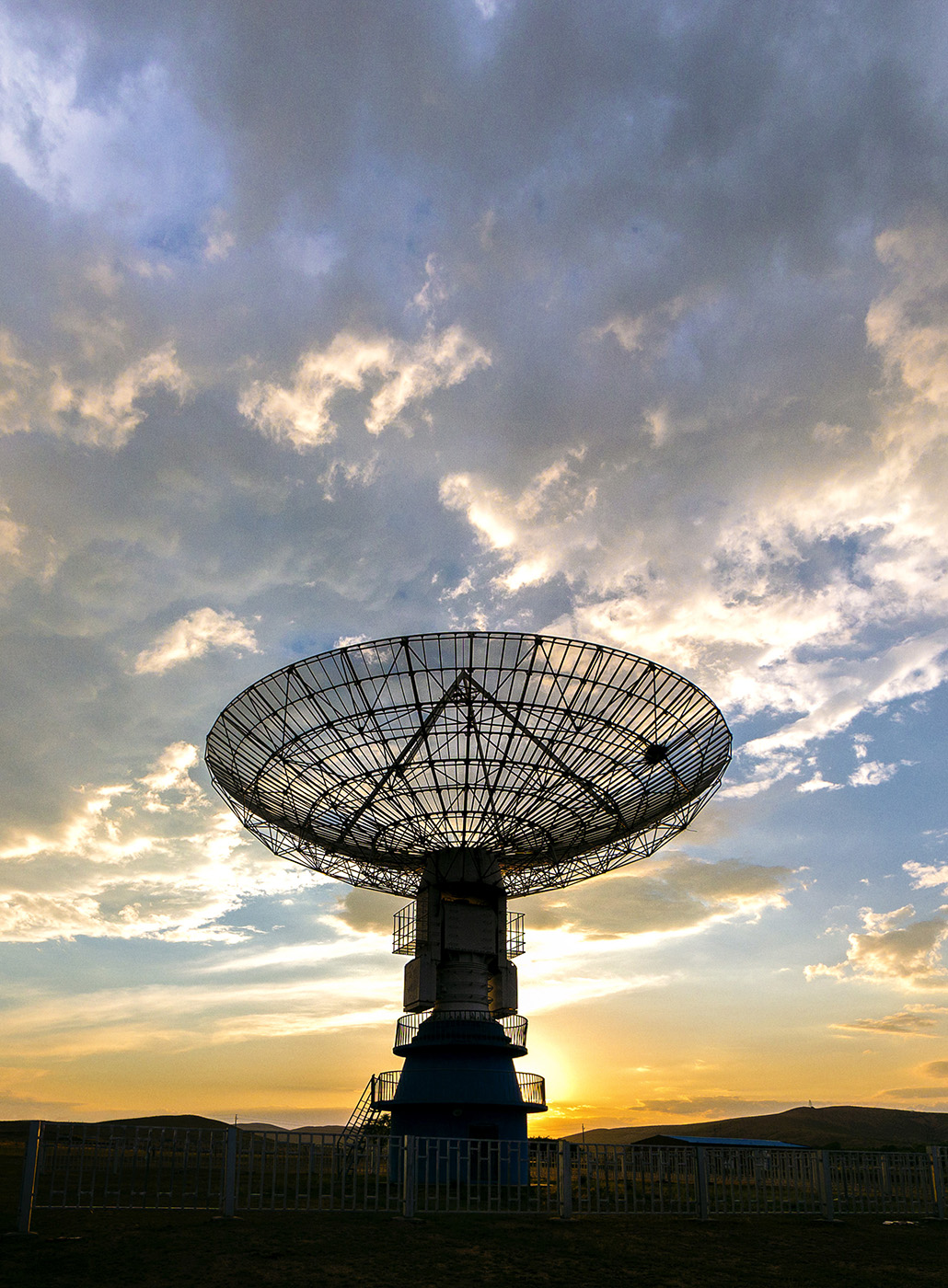 Photo of a satellite dish angled up toward the sky with sunset behind it